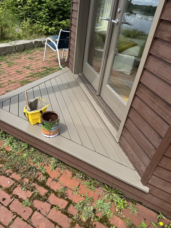 Freshly stained entry deck with the stain can and brush bucket beside the door