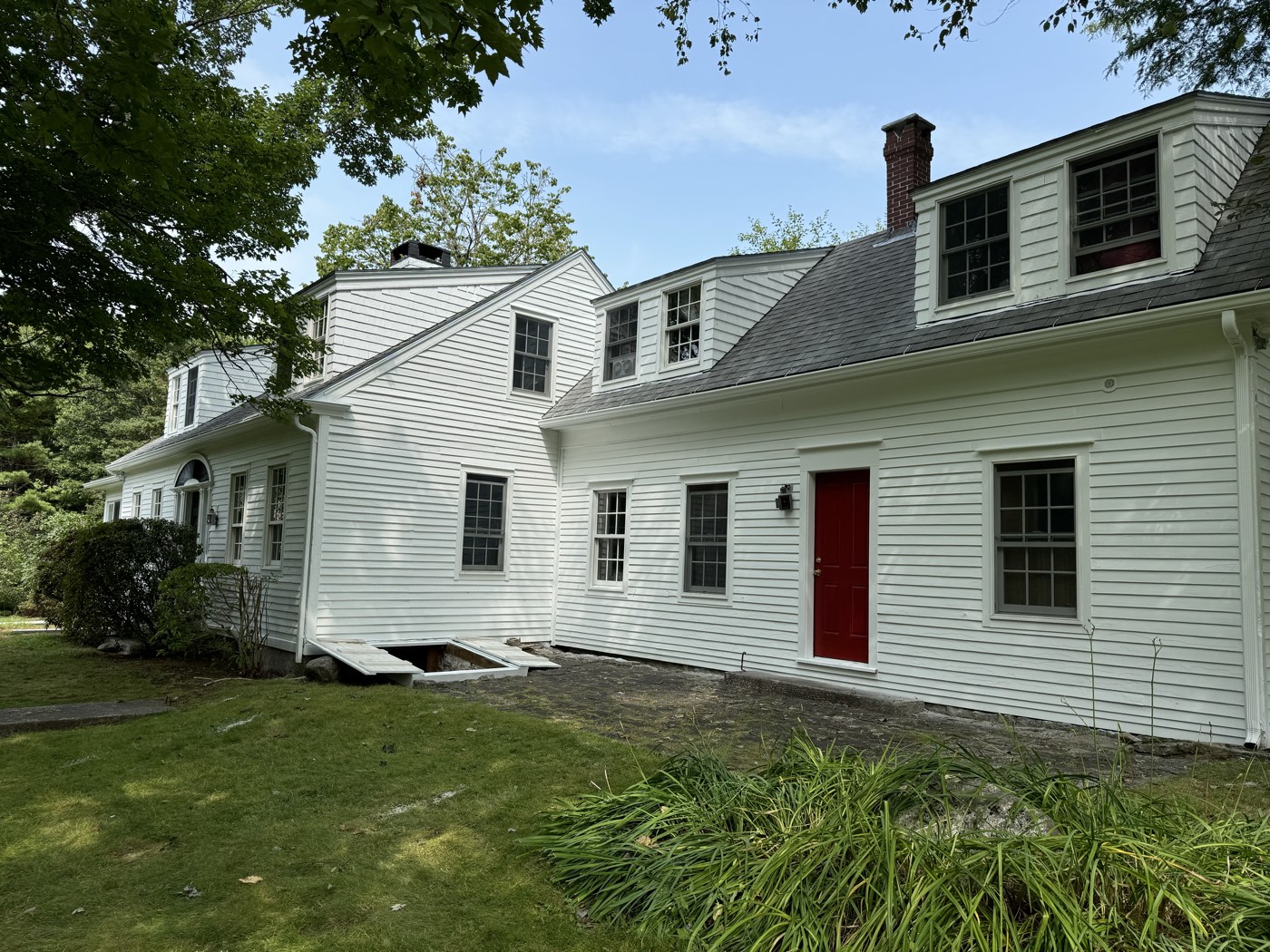 White clapboard home with dormers and a red door after a full exterior repaint