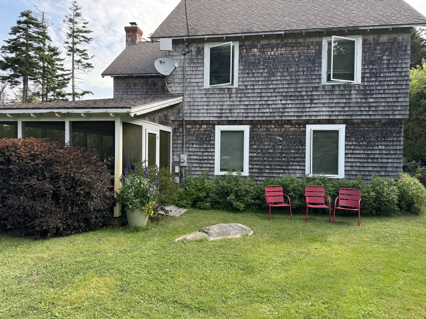 Shingled home with crisp white trim and red porch chairs