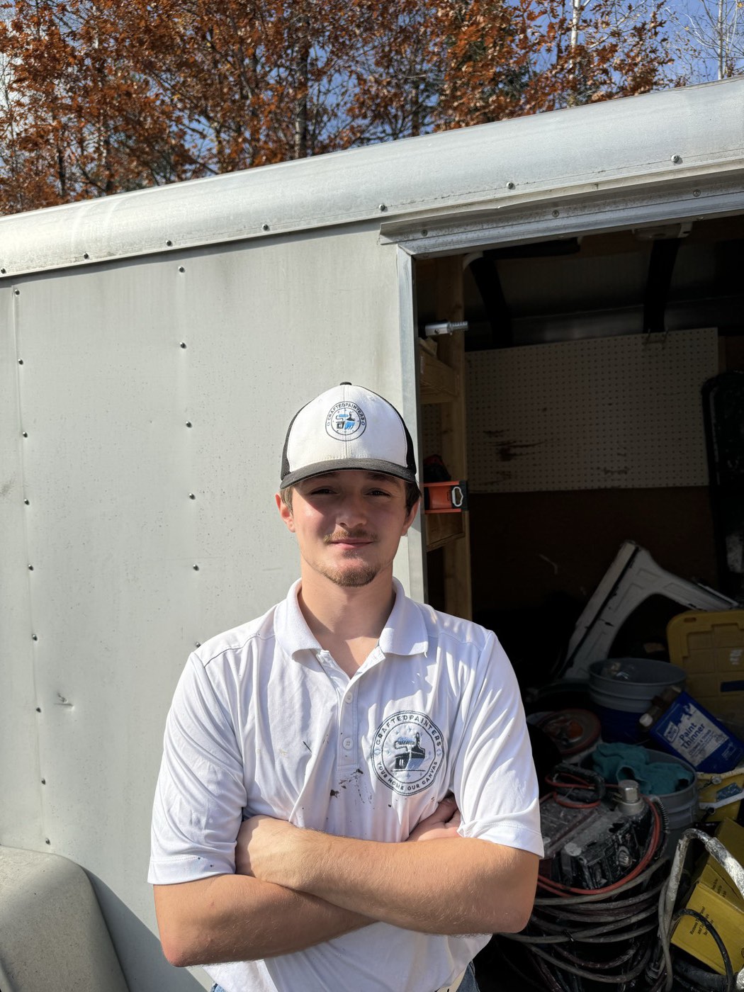 Crafted Painters team member in a company polo, arms crossed, in front of the work trailer