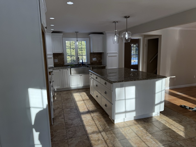 Sunlit kitchen with white cabinets, a large island and freshly painted walls