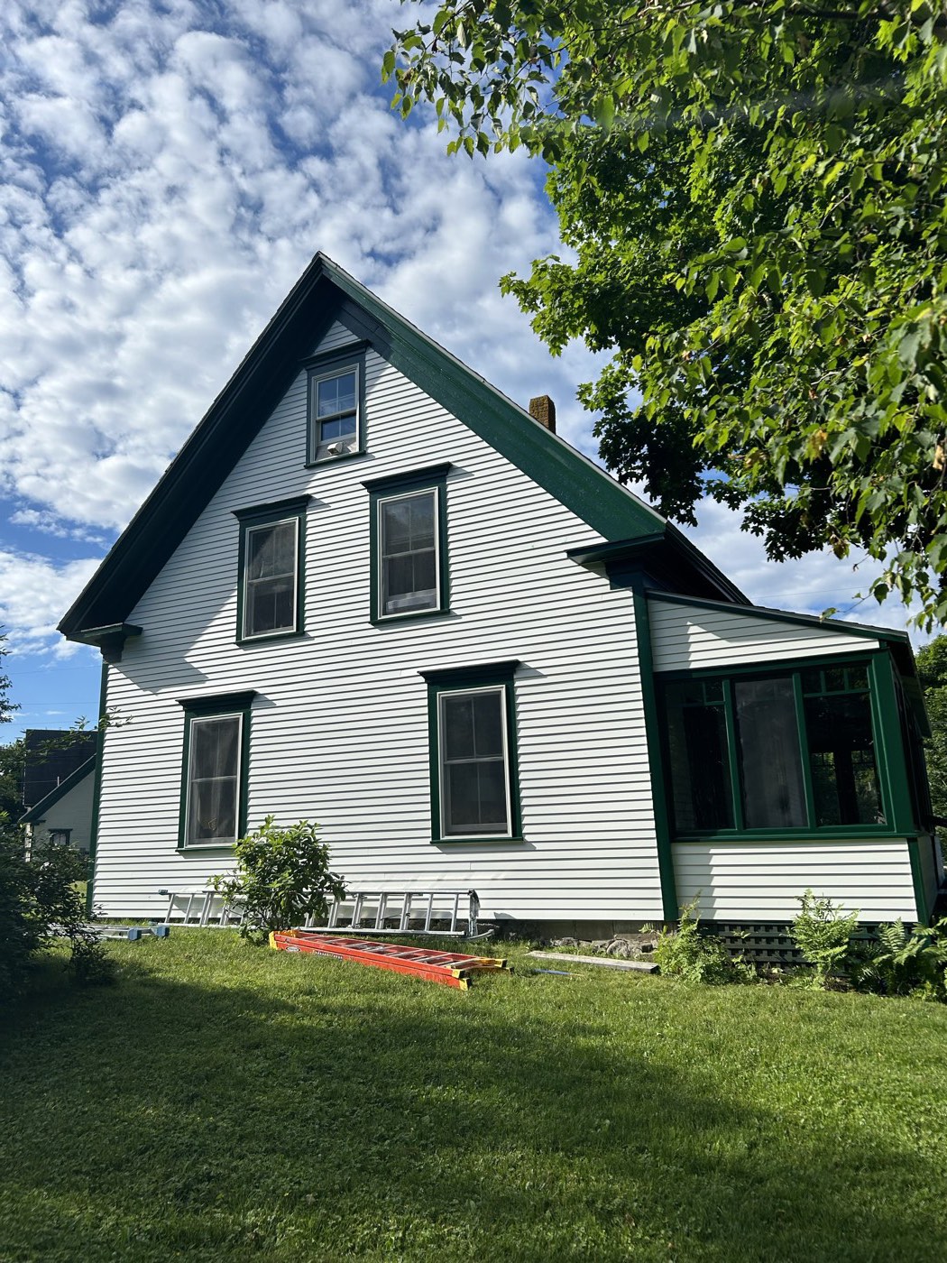 White house with dark green trim and a screened porch after exterior painting