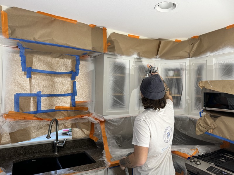 Painter spraying cabinets in a carefully masked kitchen