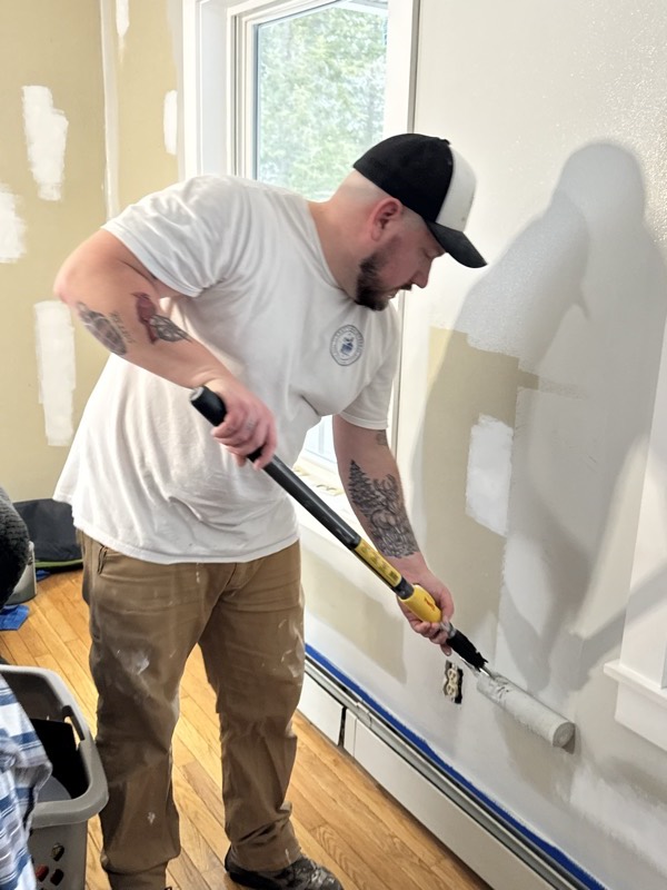 Painter rolling paint onto an interior wall with an extension pole