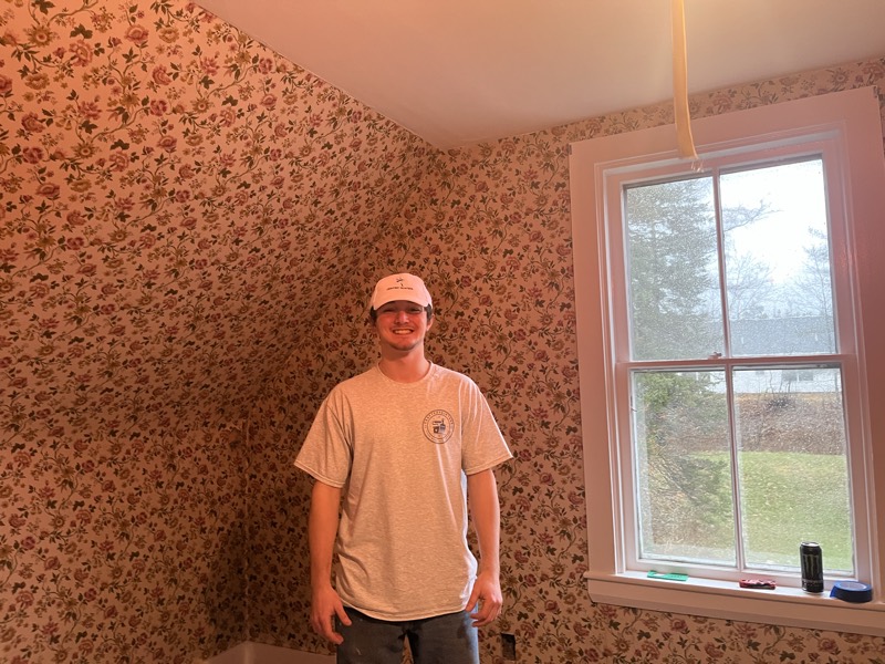 Crew member in a bedroom covered in dated floral wallpaper, with the floor protected, ready for removal