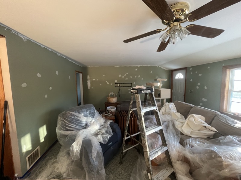 Living room with patched walls, furniture wrapped in plastic, ready for sanding and paint