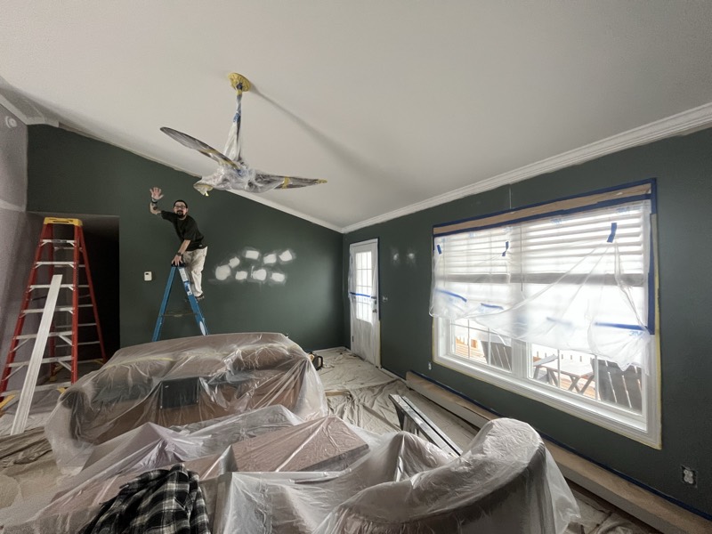 Crew patching drywall from a ladder in a vaulted room with the furniture and floor covered
