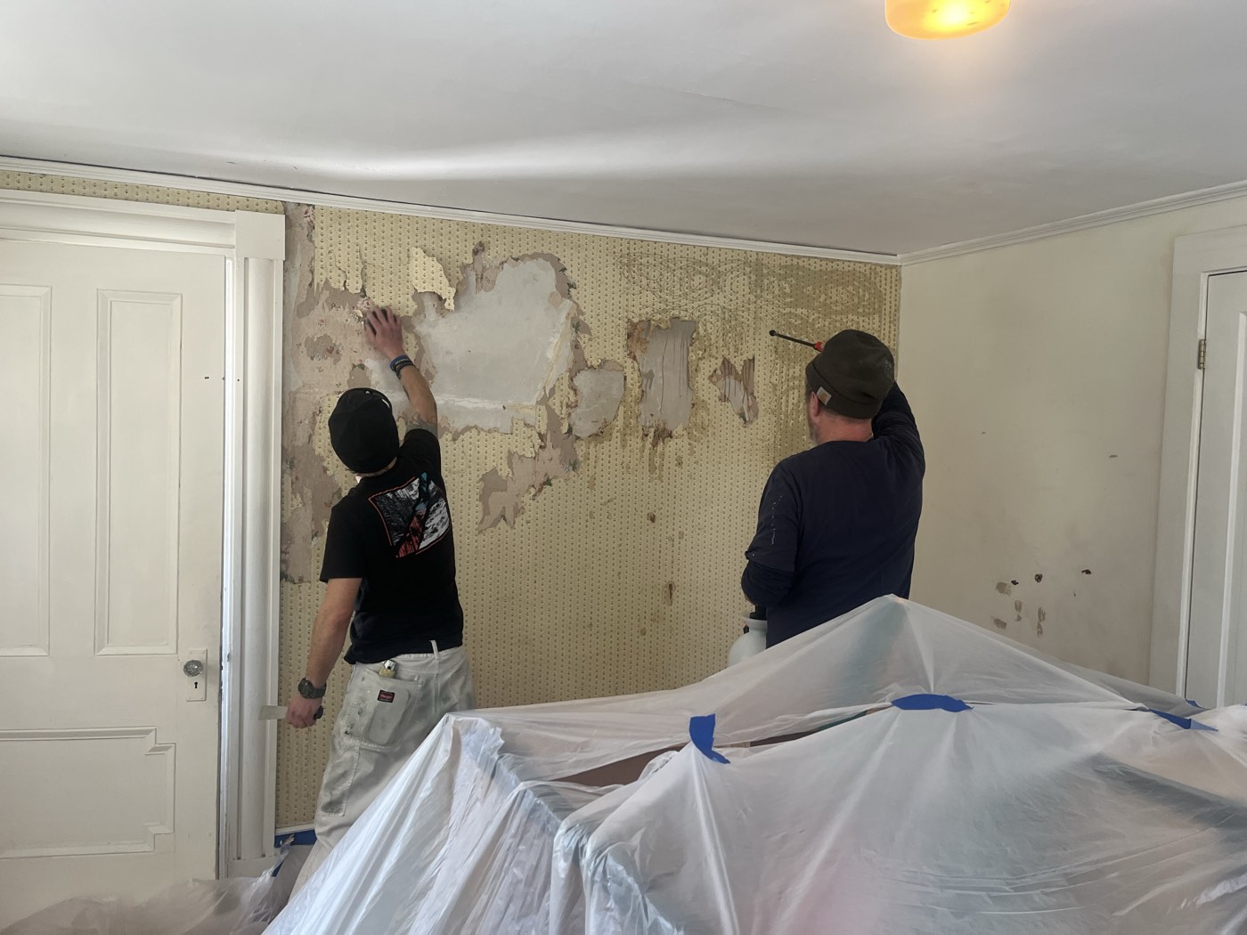 Crew stripping old wallpaper in a bedroom with floors and furniture fully protected