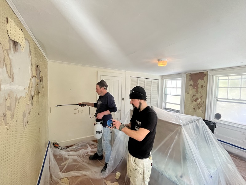 Painters removing wallpaper and adhesive in a protected bedroom