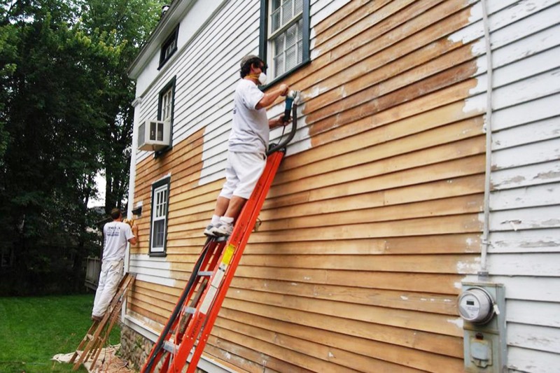 Painters on ladders sanding old paint off clapboard siding with a dust-collecting sander